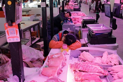Người bán thịt heo tại Bắc Kinh chợp mắt trong lúc chờ khách vào tháng 10/2019. Ảnh: Wu Hong
