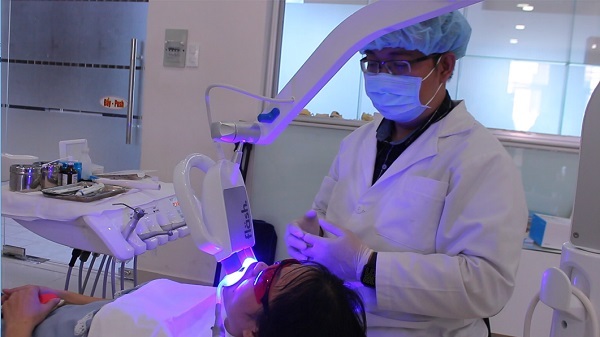 Bác sĩ Nguyễn Quang Tâm đang thực hiện tẩy trắng răng cho bệnh nhân. Ảnh: Lê Cầm