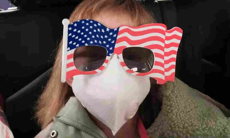 Hermione đeo khẩu trang và kính hình cờ Mỹ khi ngồi xe tới sân bay gần Vũ Hán hôm 28/1. Ảnh: AP.