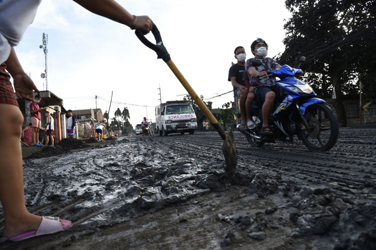Người dân ở phía nam Manila cào bùn  từ núi lửa đọng lại sau mưa ngày 13/1. Ảnh: AFP.