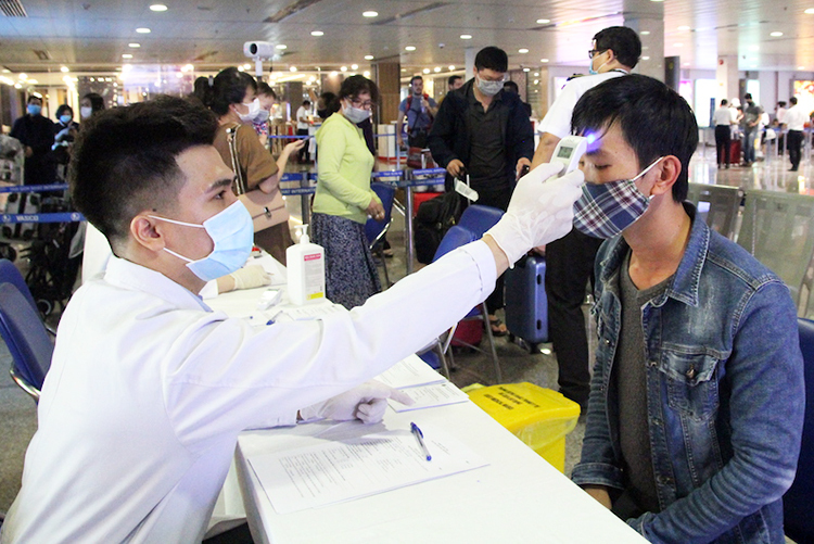 Nhân viên Trung tâm kiểm dịch quốc tế đo thân nhiệt hành khách tại sân bay Tân Sơn Nhất. Ảnh: Hữu Nguyên