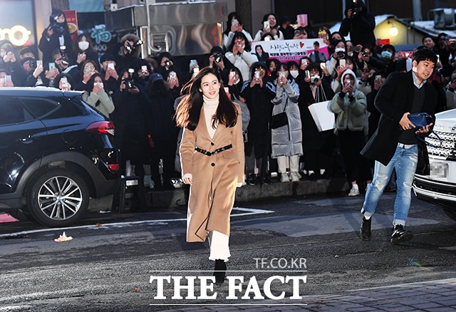 Tình đầu quốc dân của màn ảnh Hàn Son Ye Jin xuất hiện với áo cổ lọ và áo măng tô dài - một trong những kiểu trang phục quen thuộc của cô trong phim. Dưới thời tiết giá lạnh của Seoul, đông đảo người hâm mộ có mặt từ sớm để chào đón dàn diễn viên họ yêu mến.