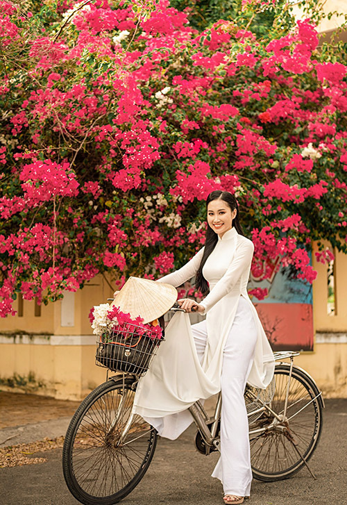 Đoàn Hồng Trang duyên dáng trong tà áo dài trắng đạp xe dạo phố khi về thăm quê. Mùa này những giàn hoa giấy đang nở rộ rực rỡ ở nhiều góc đường.