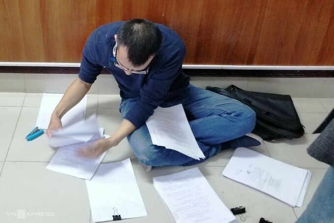 Một người dân rải số giấy tờ trên nền nhà do không còn bàn để làm thủ tục. Ảnh: Giang Chinh