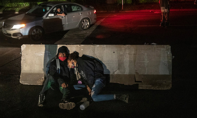 Hai người kiệt sức ngồi trên đường sau cuộc biểu tình giữa đêm ở thành phố Minneapolis cuối tuần qua. Ảnh: NYTimes.