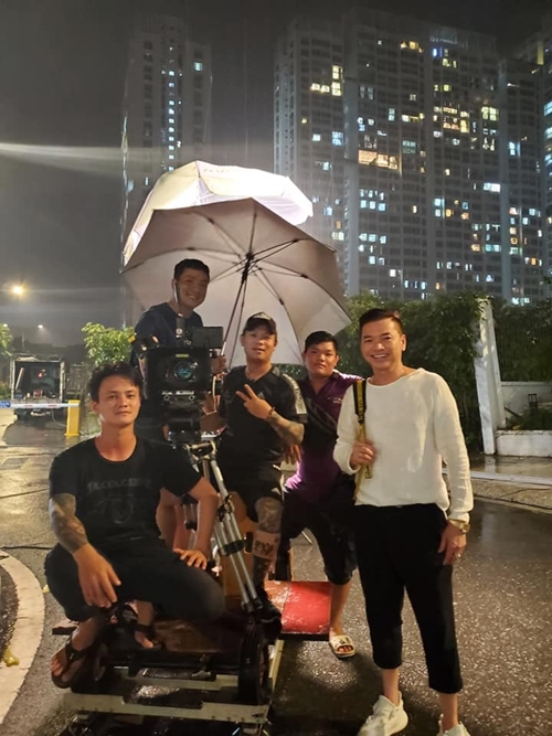 Nghệ sĩ Quang Minh cùng êkíp trong cảnh quay trời mưa. Phim Sugar Daddy và Sugar Baby dài năm tập, dự kiến trình chiếu trong thời gian tới.