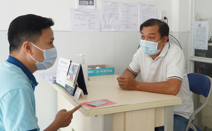 Anh Phú (bên phải) giải đáp thắc mắc khi người dân đến trạm y tế xin giấy chứng nhận không đến từ vùng dịch để về quê. Ảnh: Thư Anh.